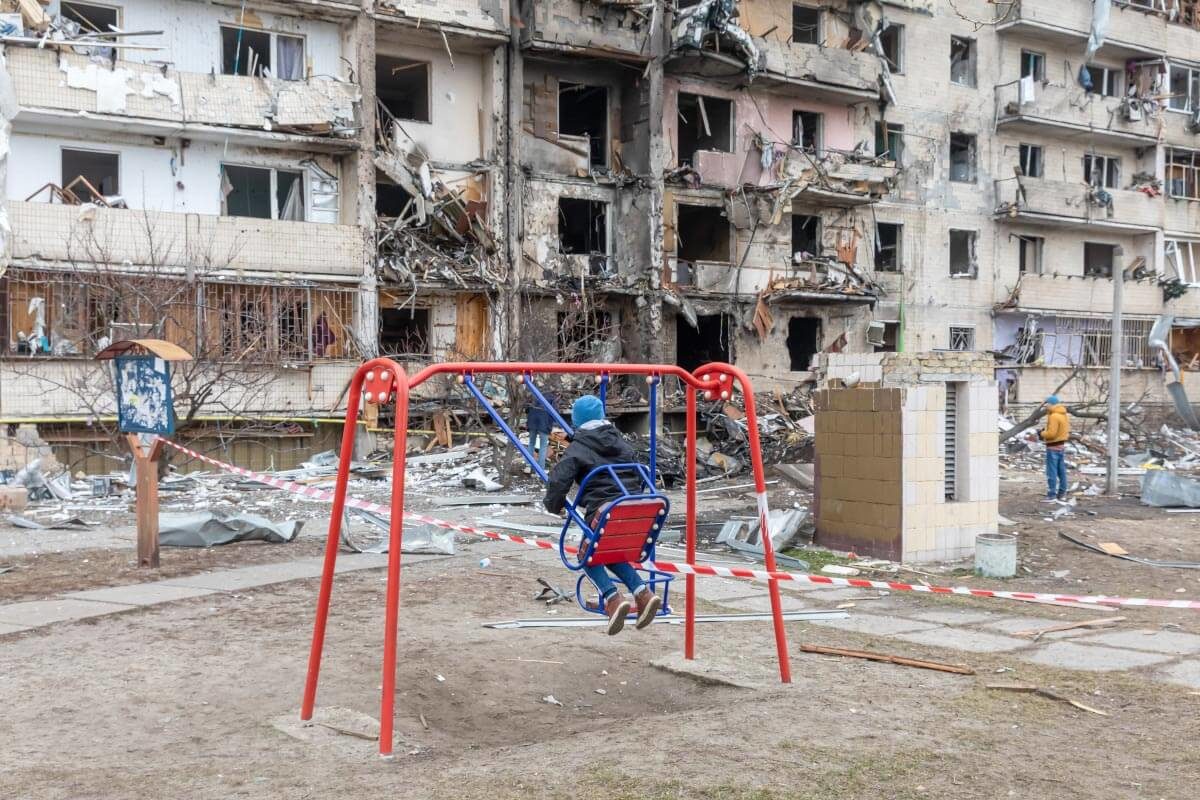 Child swinging in front of a bombed building in Kyiv, Ukraine