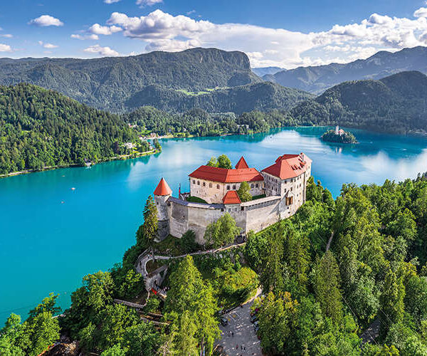 Castle on a grassy hill next to a crystal blue lake