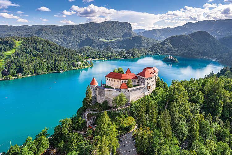 Castle on a grassy hill next to a crystal blue lake