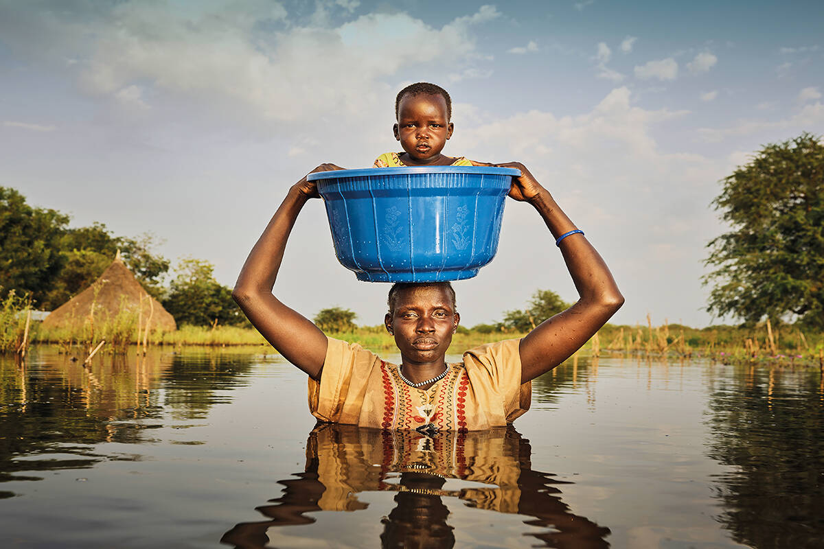 A woman holds her child above her in the flood waters in a bucket