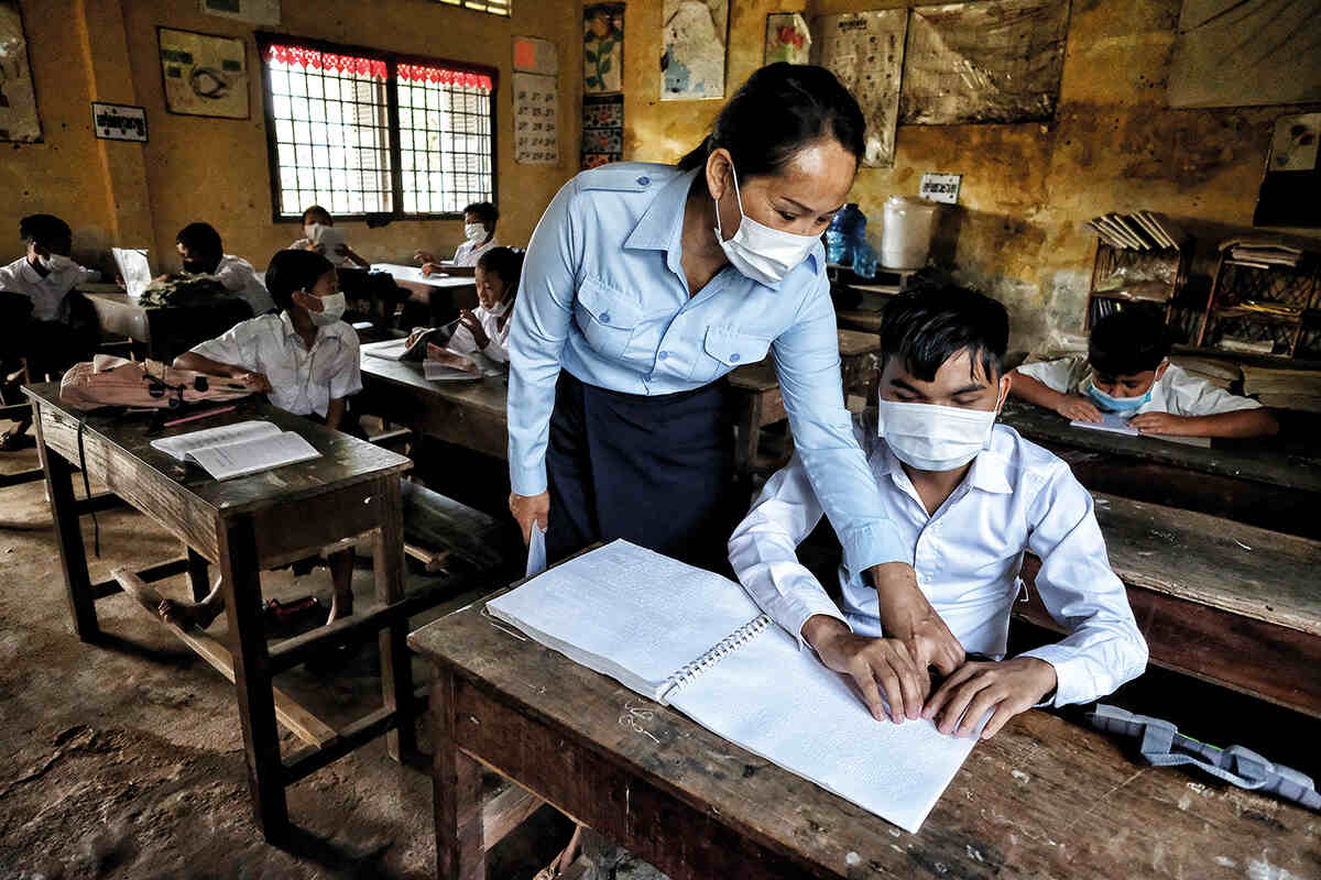 Teacher pointing in a textbook leaning over a student 