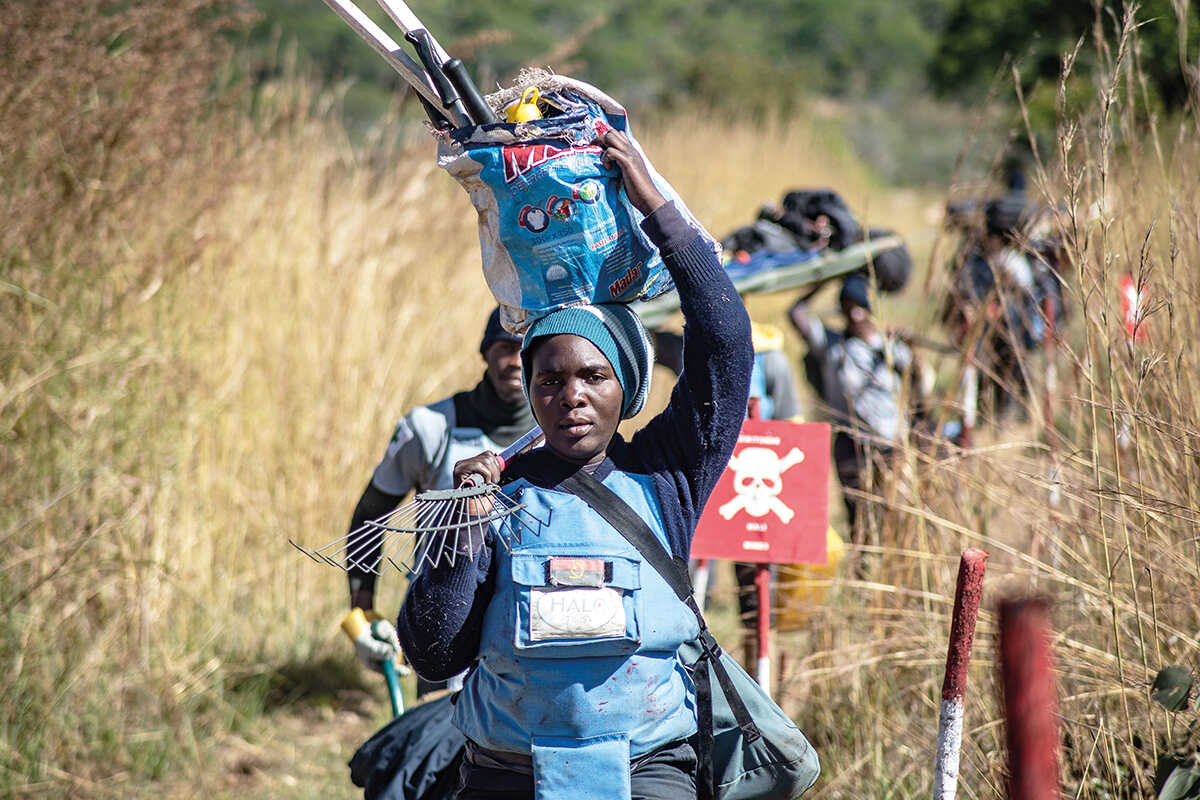 A line of people carry de-mining equipment