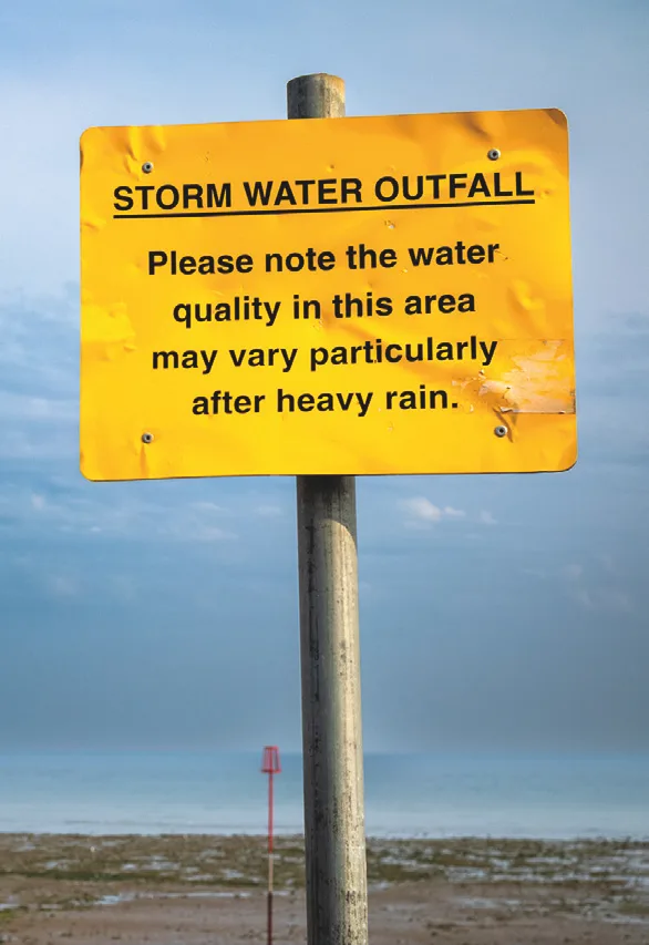 Yellow storm water outfall warning sign on a beach at Worthing